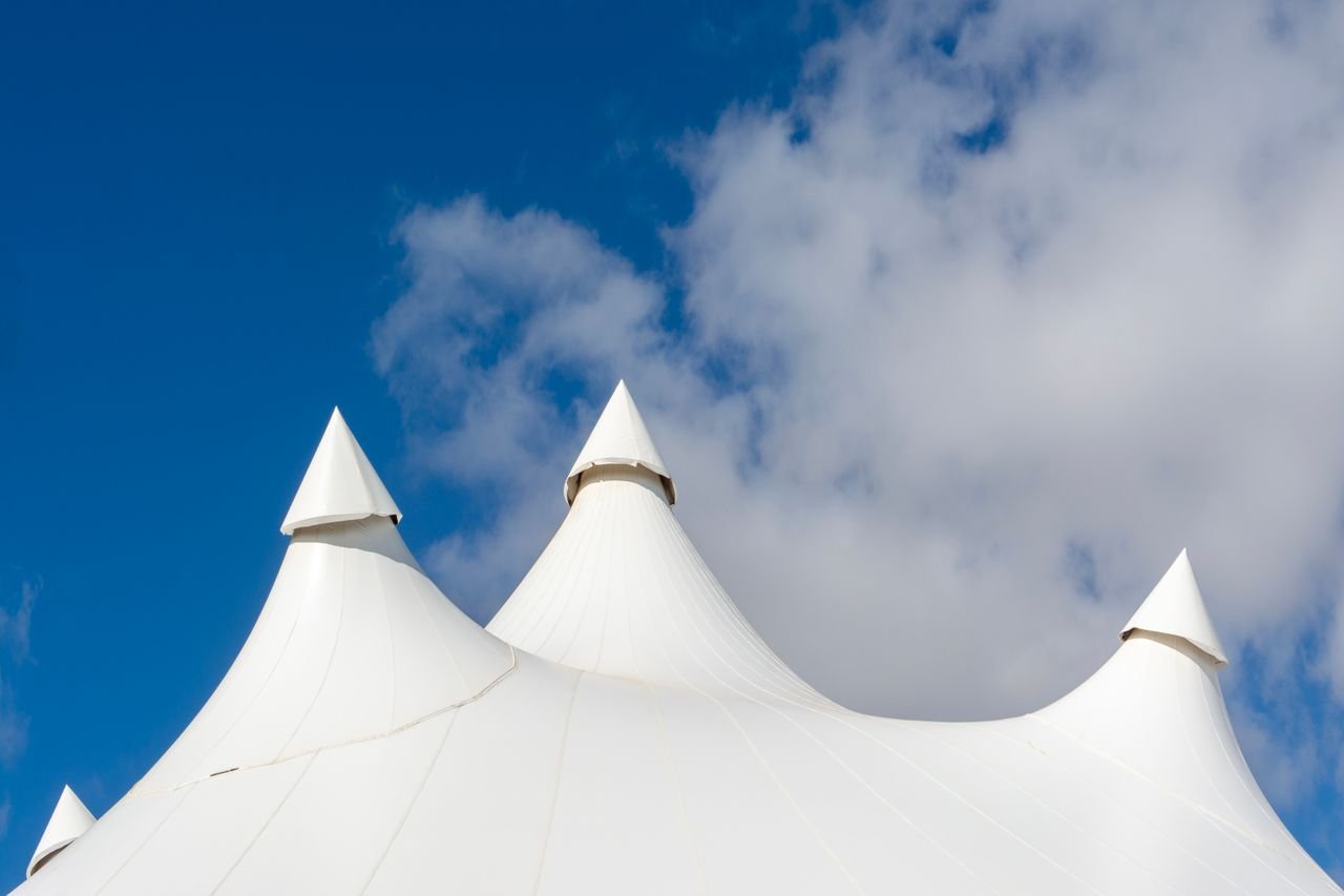 services-03 Elegant white tent peaks under a bright blue sky with scattered clouds.